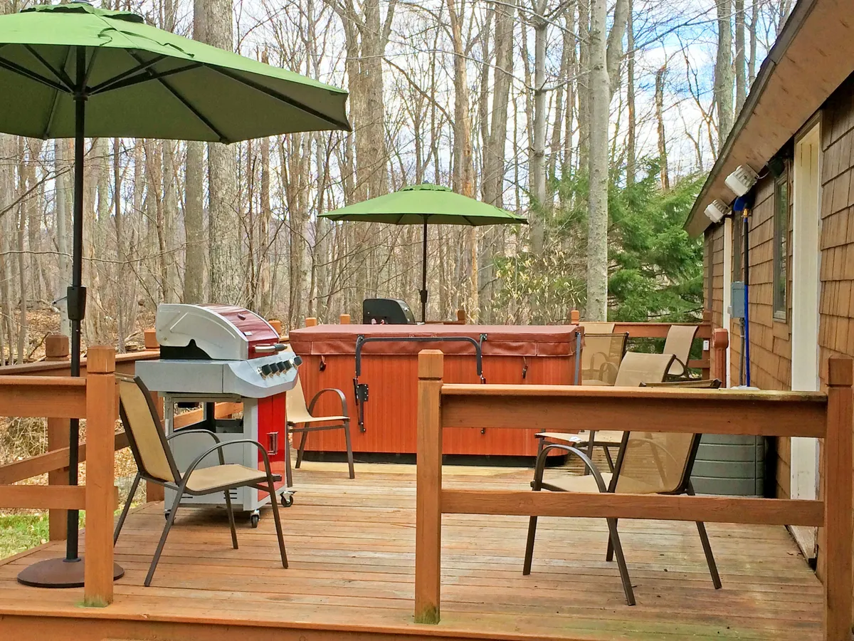 This exterior shot features a spacious deck with a grill, outdoor seating, umbrellas, and a hot tub. It conveys an inviting atmosphere for barbecues, family gatherings, and post-adventure relaxation while immersed in the mountain landscape.