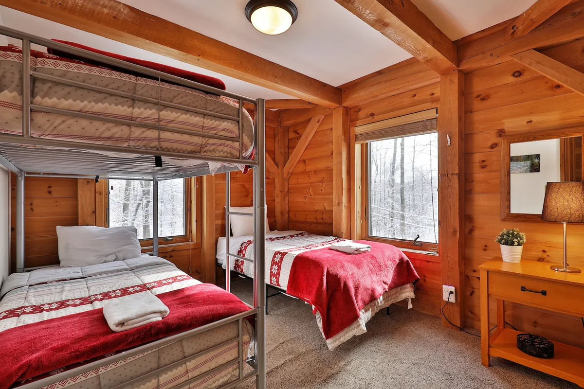 The room contains a bunk bed and a single bed, windows looking out at a snowy landscape, and cozy wooden furnishings. The room exudes a sense of warmth and togetherness, ideal for family stays or group getaways.
