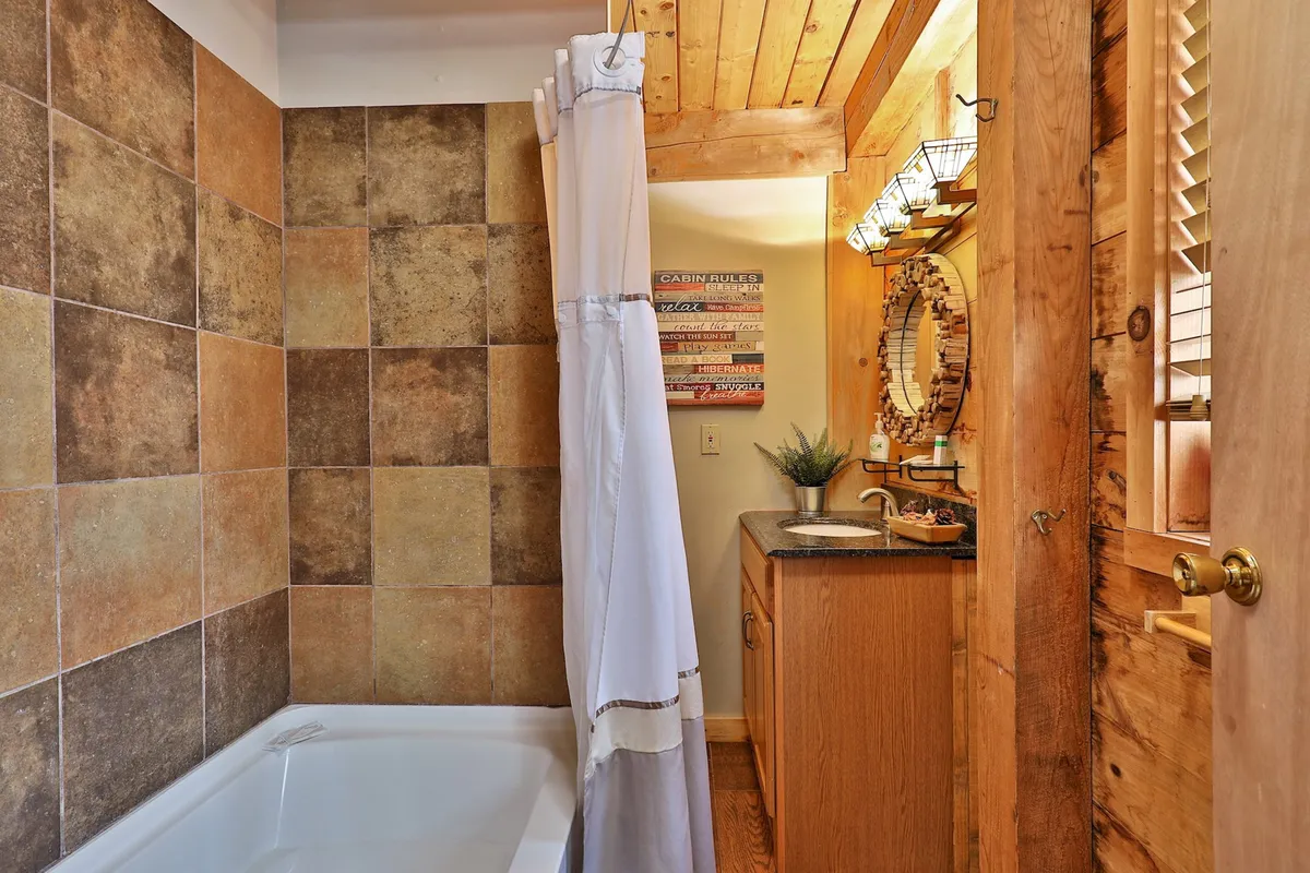 A stylish bathroom with a bathtub, textured wall tiles, wooden ceiling, and a vanity with a mirror—combining rustic charm with modern comforts for a relaxing experience.