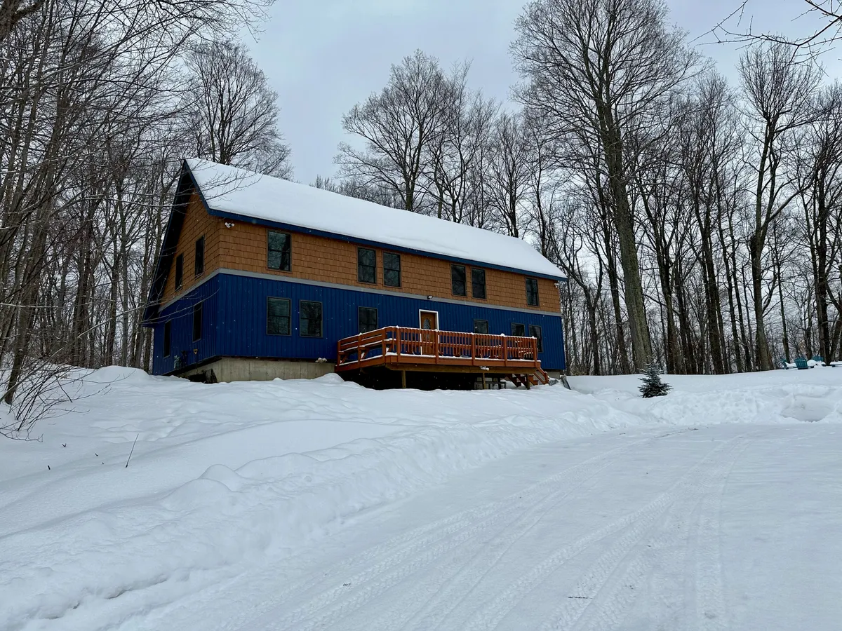 The exterior of a blue and brown house with a spacious wooden deck overlooking a snowy backyard. The image exudes coziness with hints of activity, like family gatherings or watching snow fall from the porch, and shows how the outdoor space extends the living area.